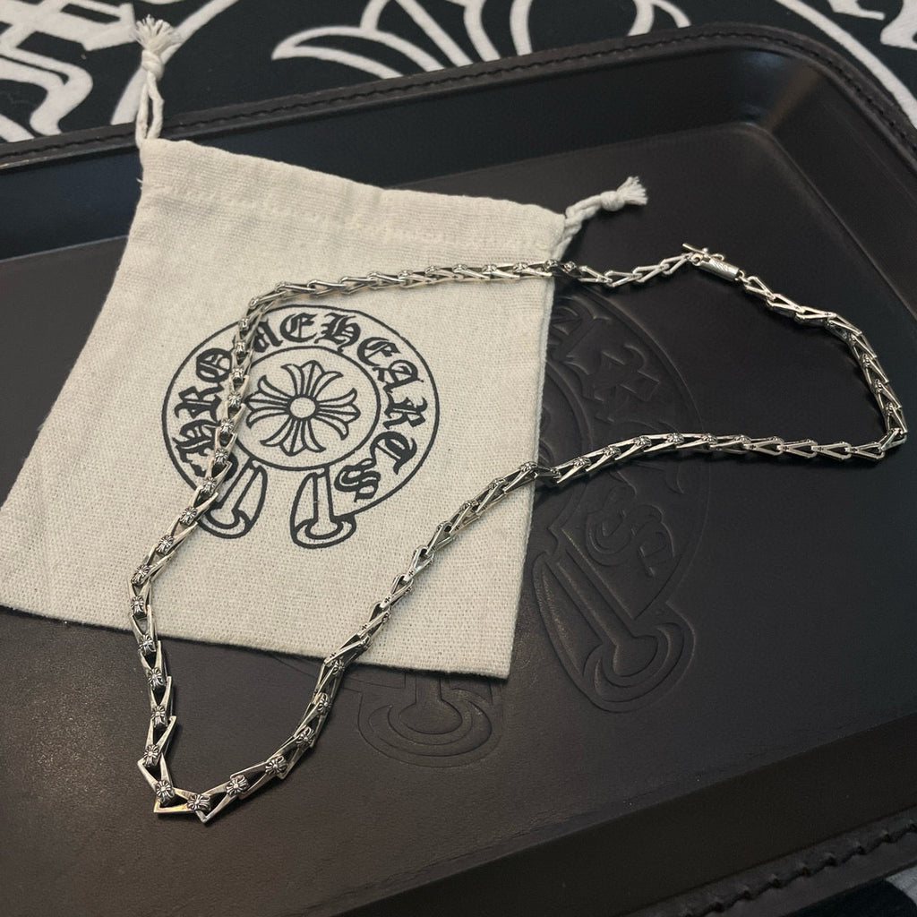 Silver-tone chain necklace resting on a dark leather box and light fabric pouch