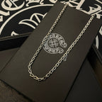 Silver-tone chain necklace on a black jewelry box with circular logo emblem