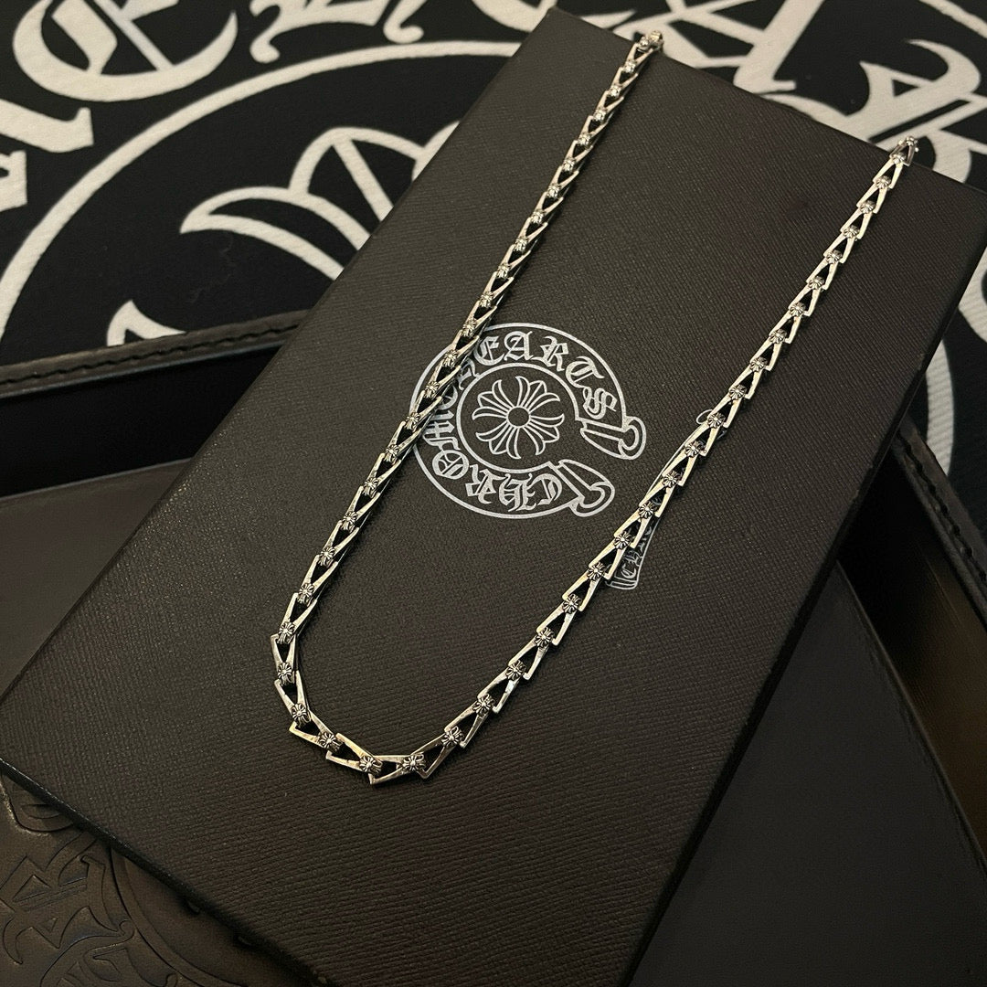 Silver-tone chain necklace on a black jewelry box with circular logo emblem