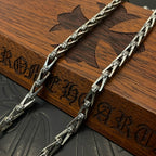 Silver-tone chain necklace laid across a brown wooden block display