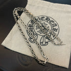 Silver-tone chain necklace laid over a light fabric pouch with dark emblem