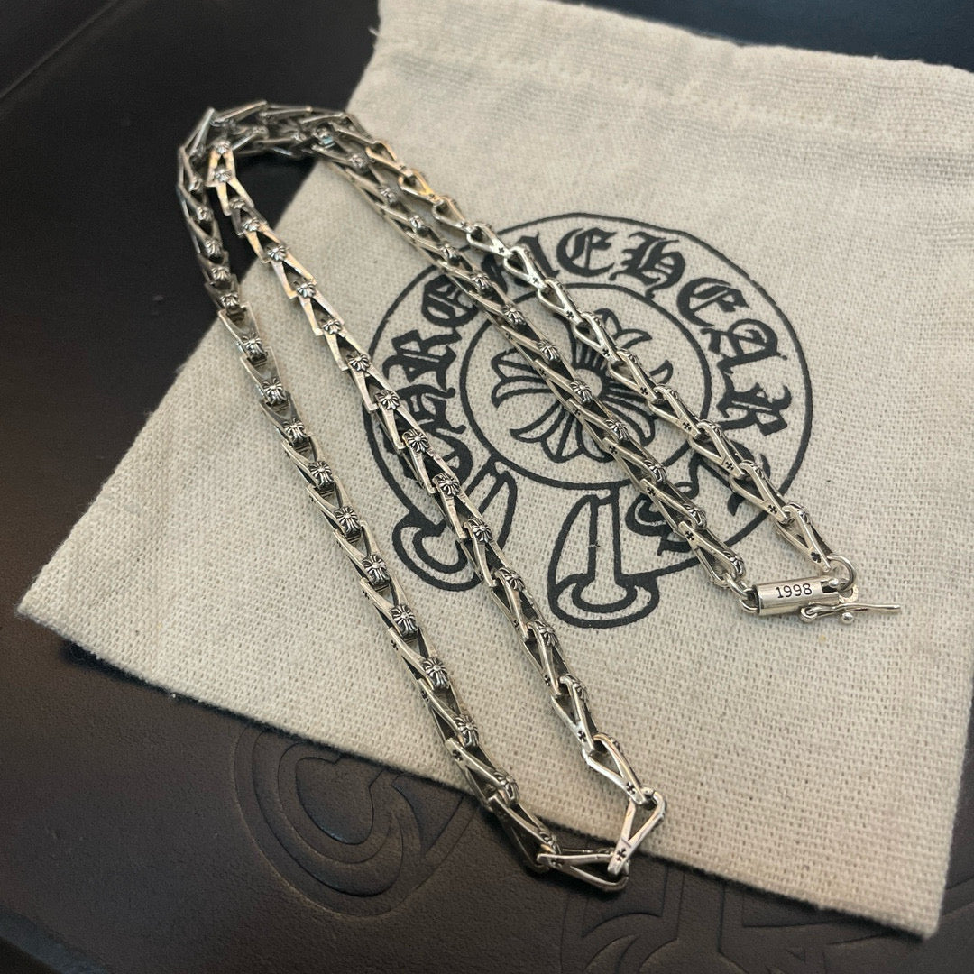 Silver-tone chain necklace laid over a light fabric pouch with dark emblem