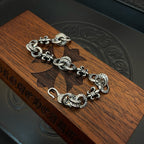 Silver-tone charm bracelet laid on wooden surface, clasp and medallion charms visible
