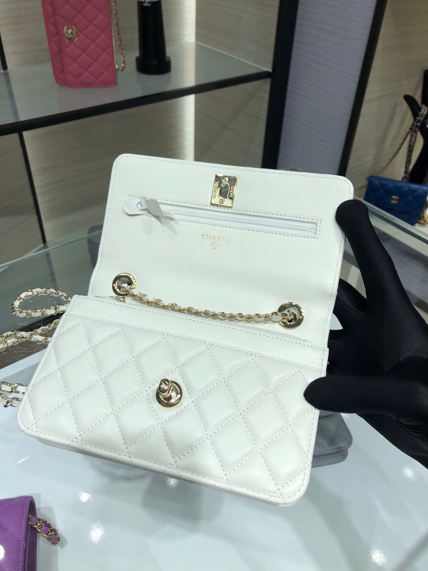 White quilted flap bag with gold chain strap and front turn-lock logo, close-up