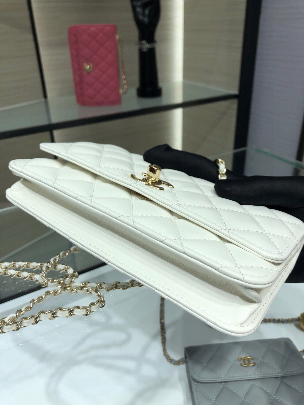 White quilted flap bag with gold logo turn-lock and chain strap, side view
