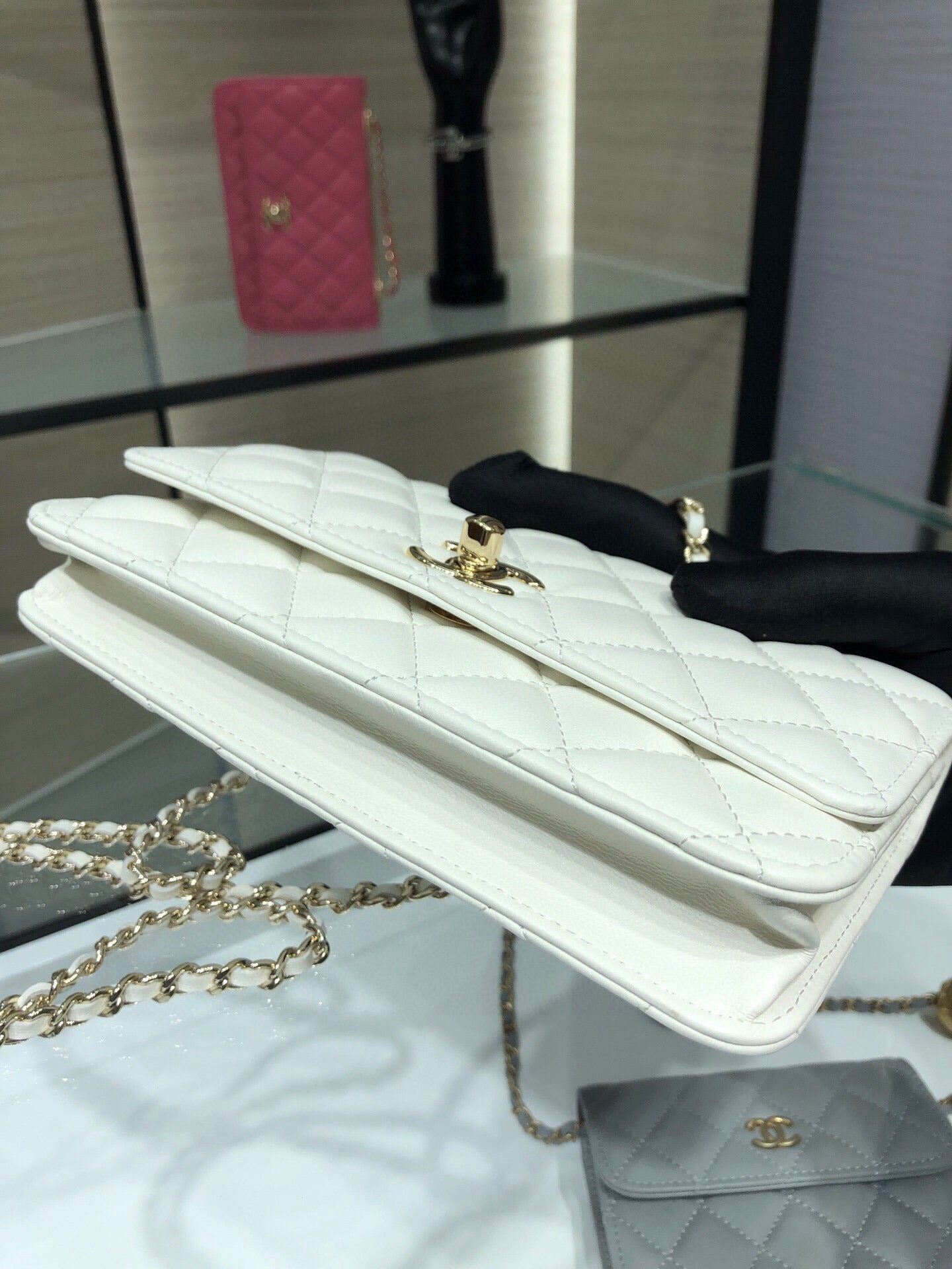 White quilted flap bag with gold logo turn-lock and chain strap, side view