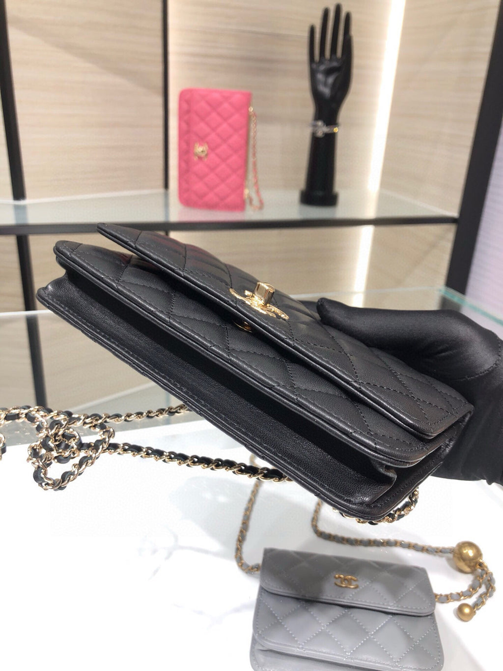 Black quilted shoulder bag with top flap and chain strap, held in hand
