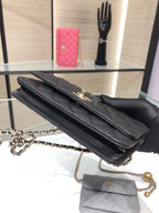 Black quilted shoulder bag with top flap and chain strap, held in hand