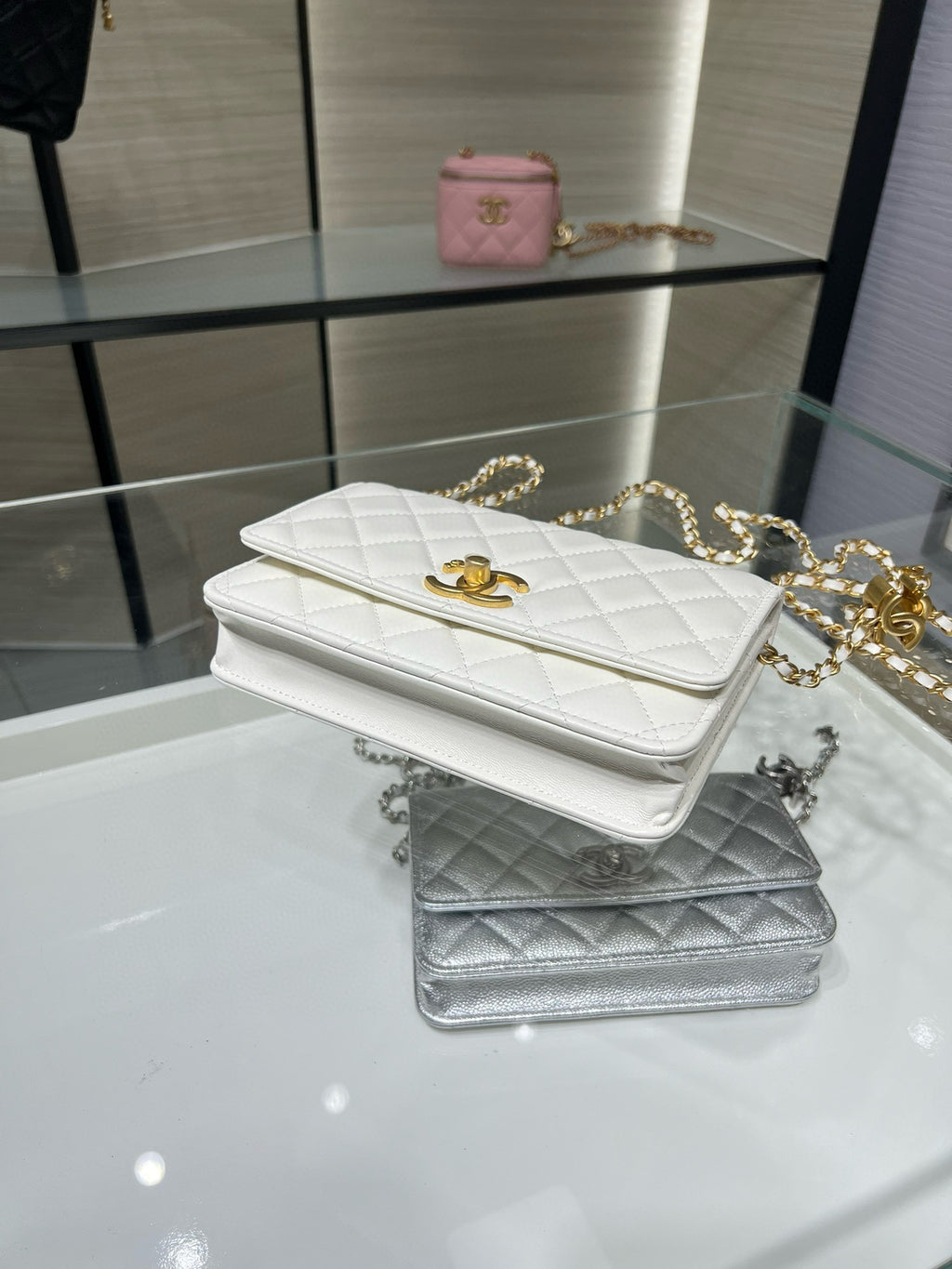 White quilted Chanel flap bag with gold hardware, plus a silver quilted bag beside it