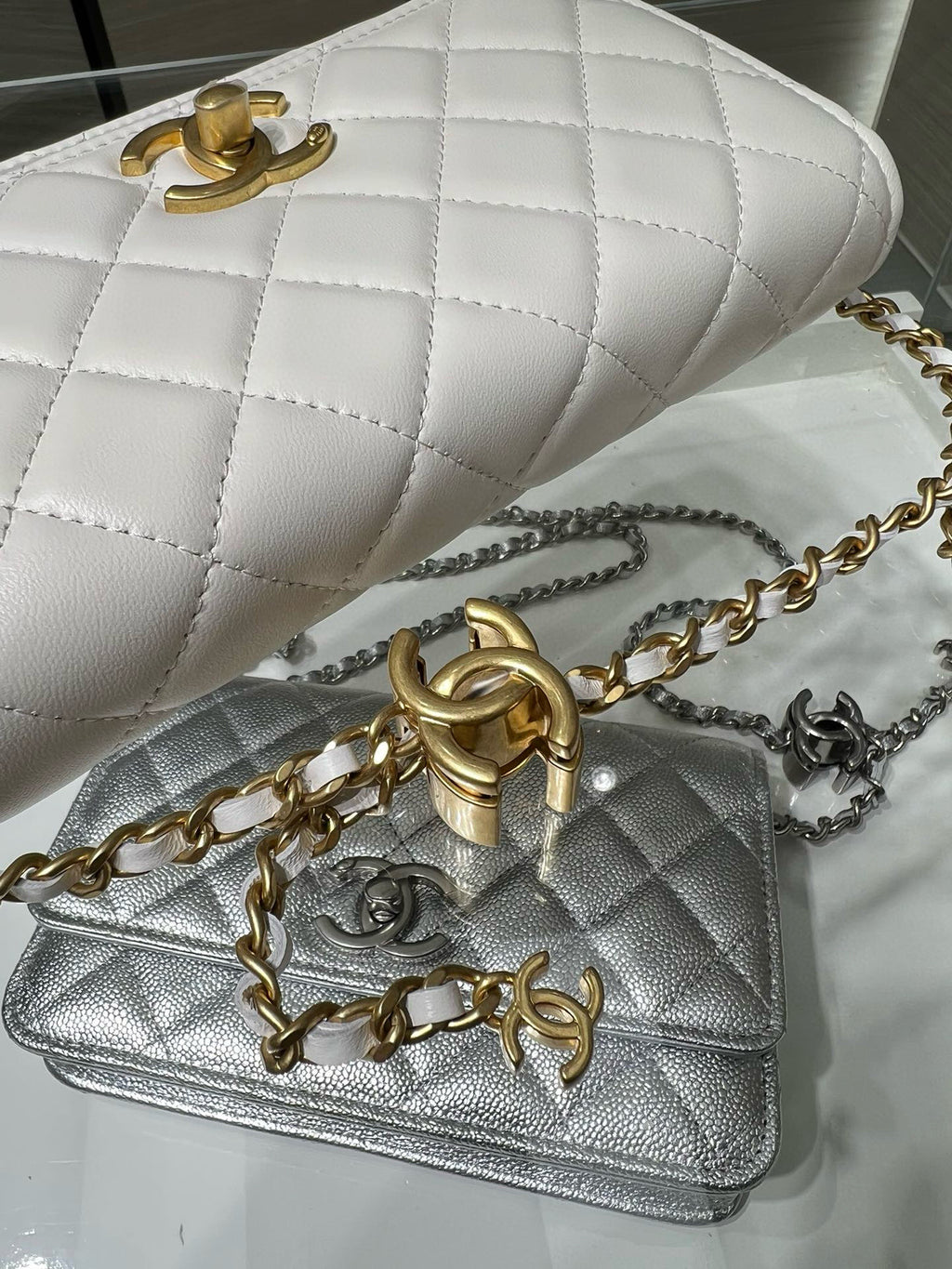 White quilted Chanel bag with gold hardware and chain strap; silver quilted bag underneath