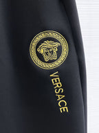 Versace black jogger pants showing gold Versace logo patch on side.