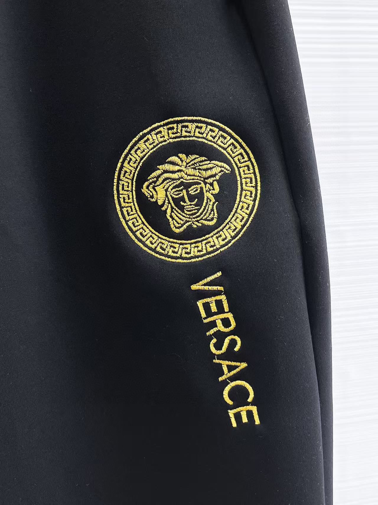 Versace black jogger pants showing gold Versace logo patch on side.
