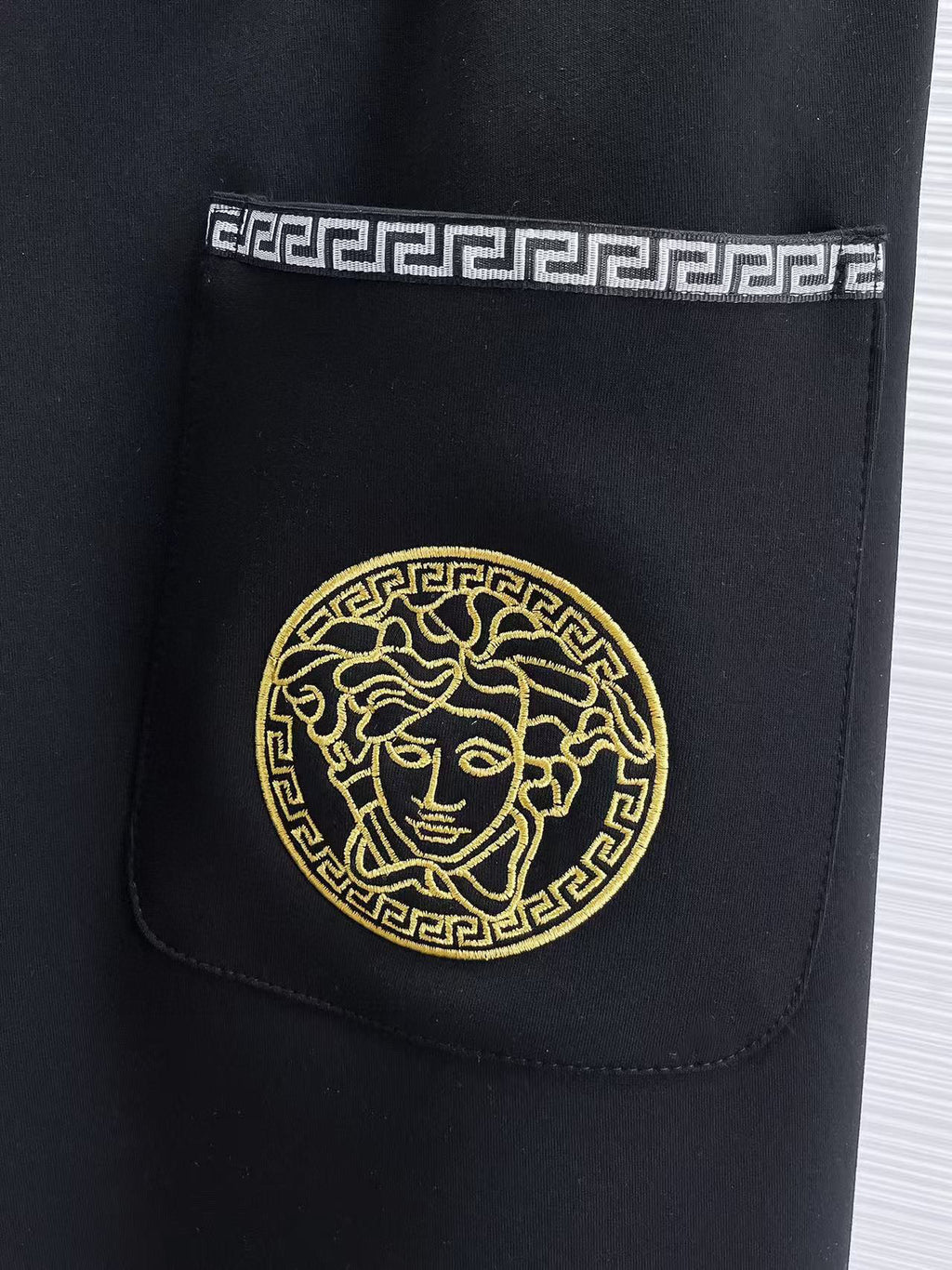 Versace black jogger pants with gold medallion emblem on front pocket.