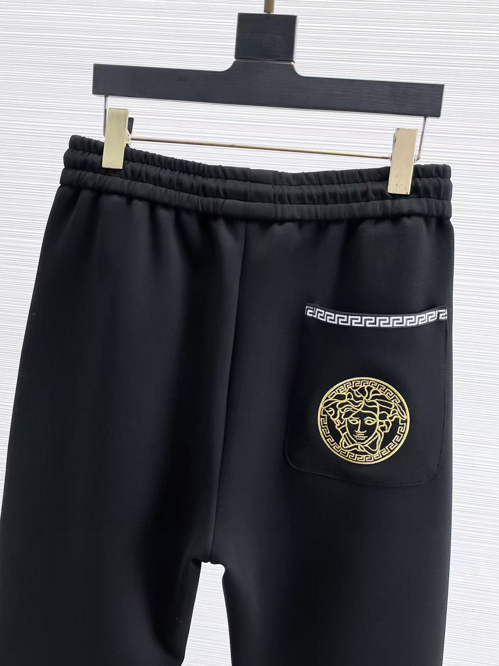 Versace black jogger pants with elastic waist, gold patterned stripe and pocket emblem.