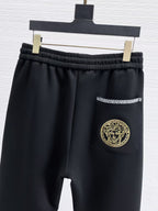 Versace black jogger pants with elastic waist, gold patterned stripe and pocket emblem.