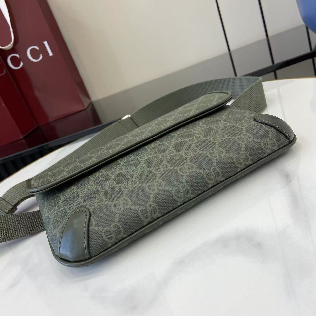 Gucci bag with GG monogram canvas, green, laid on table with long strap.