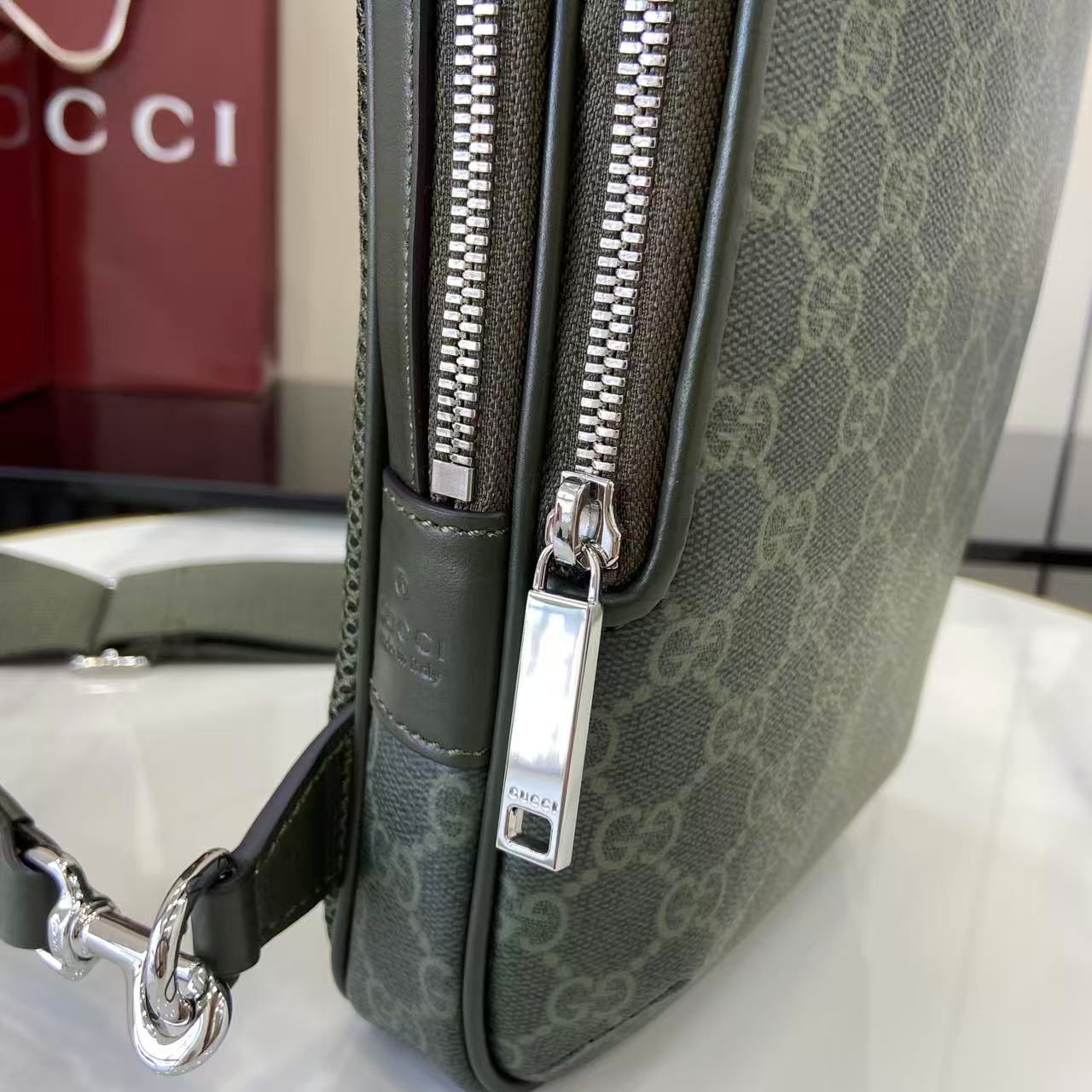 Gucci bag close-up: dark green monogram front with zip pull and silver logo plate