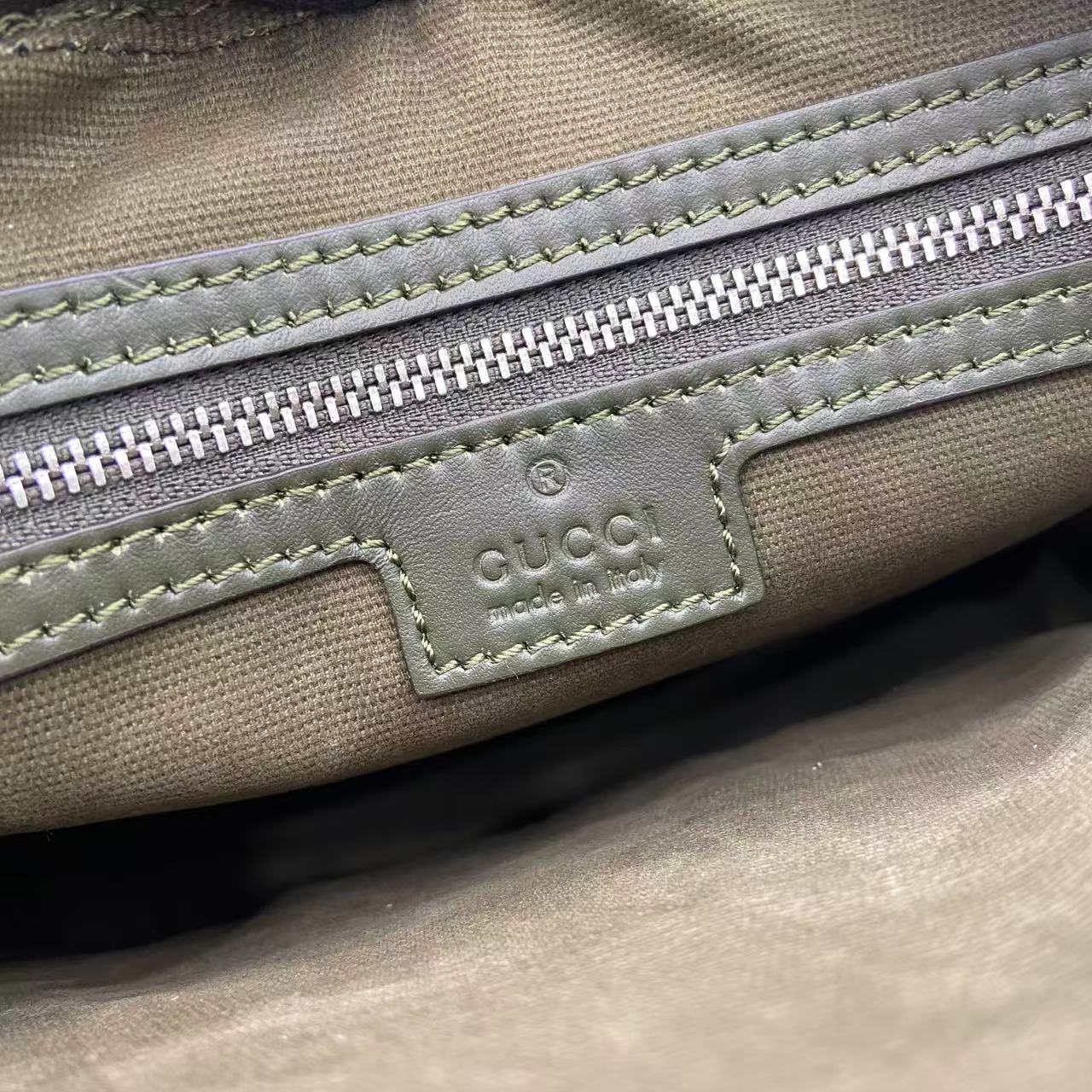 Monogram bag close-up of front logo patch, zipper, and contrast stitching