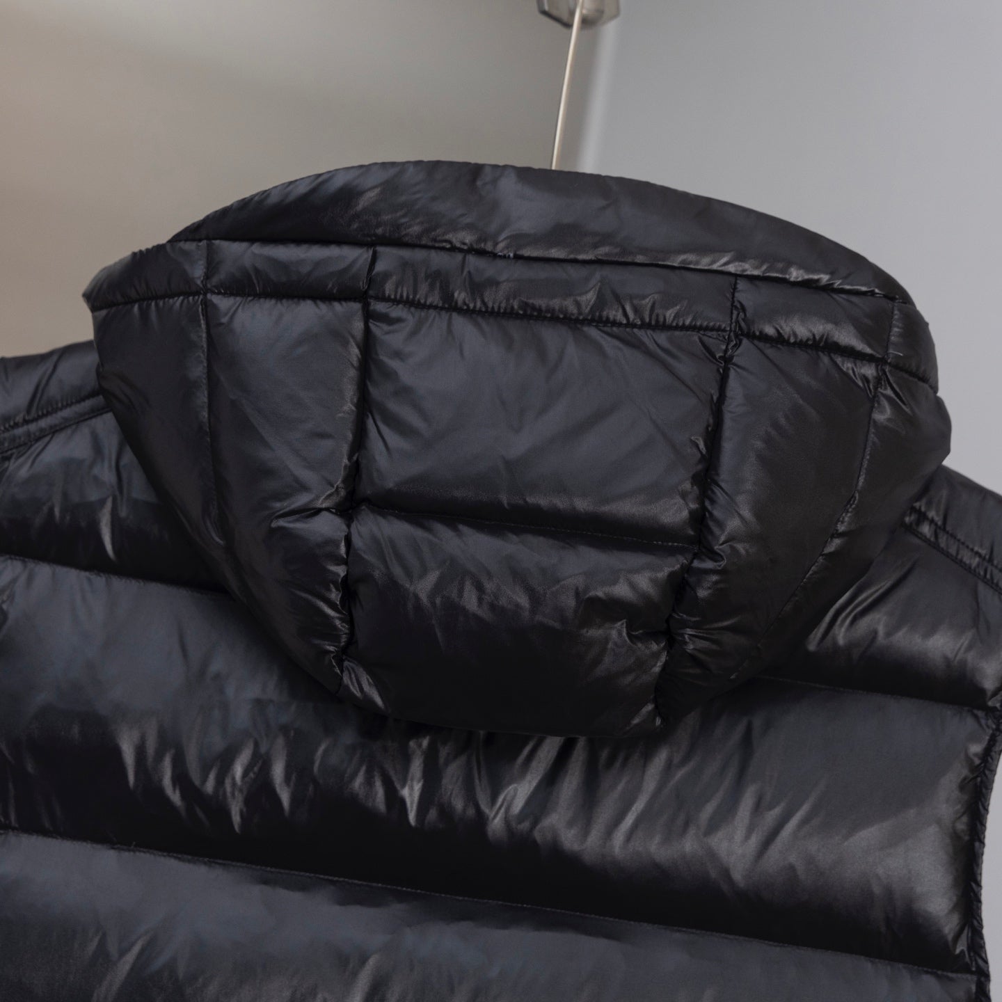 Black quilted long puffer vest close-up with horizontal baffles and hood