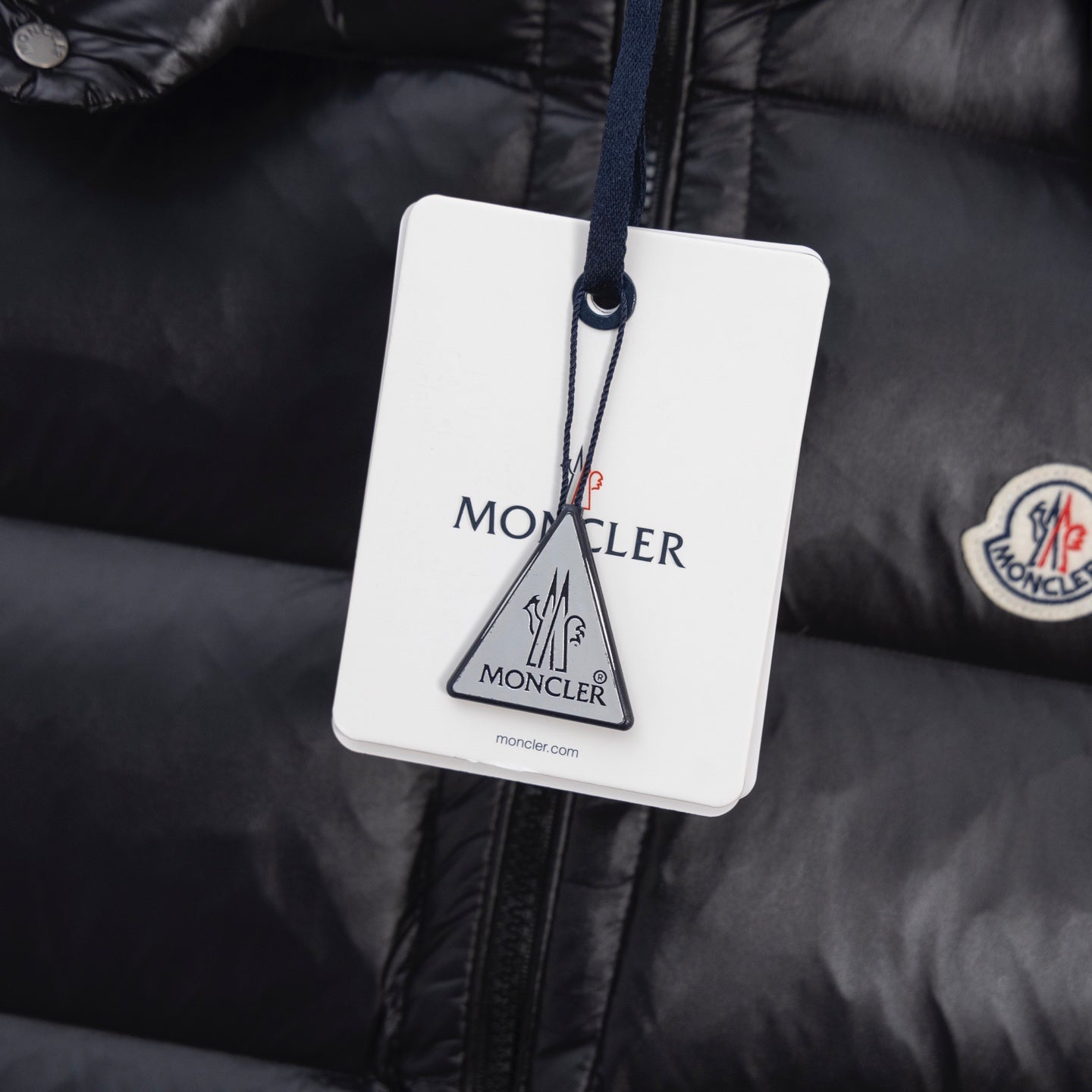 Black puffer vest fabric close-up with circular Moncler logo patch and tag