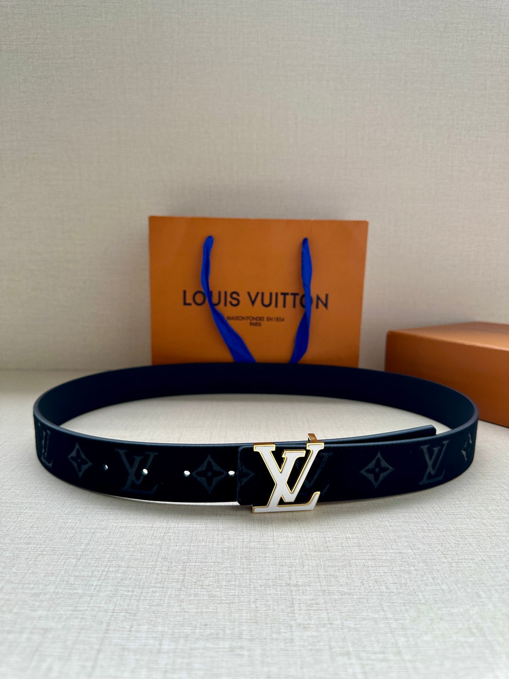 Dark navy leather belt with repeating monogram pattern and gold-tone center buckle