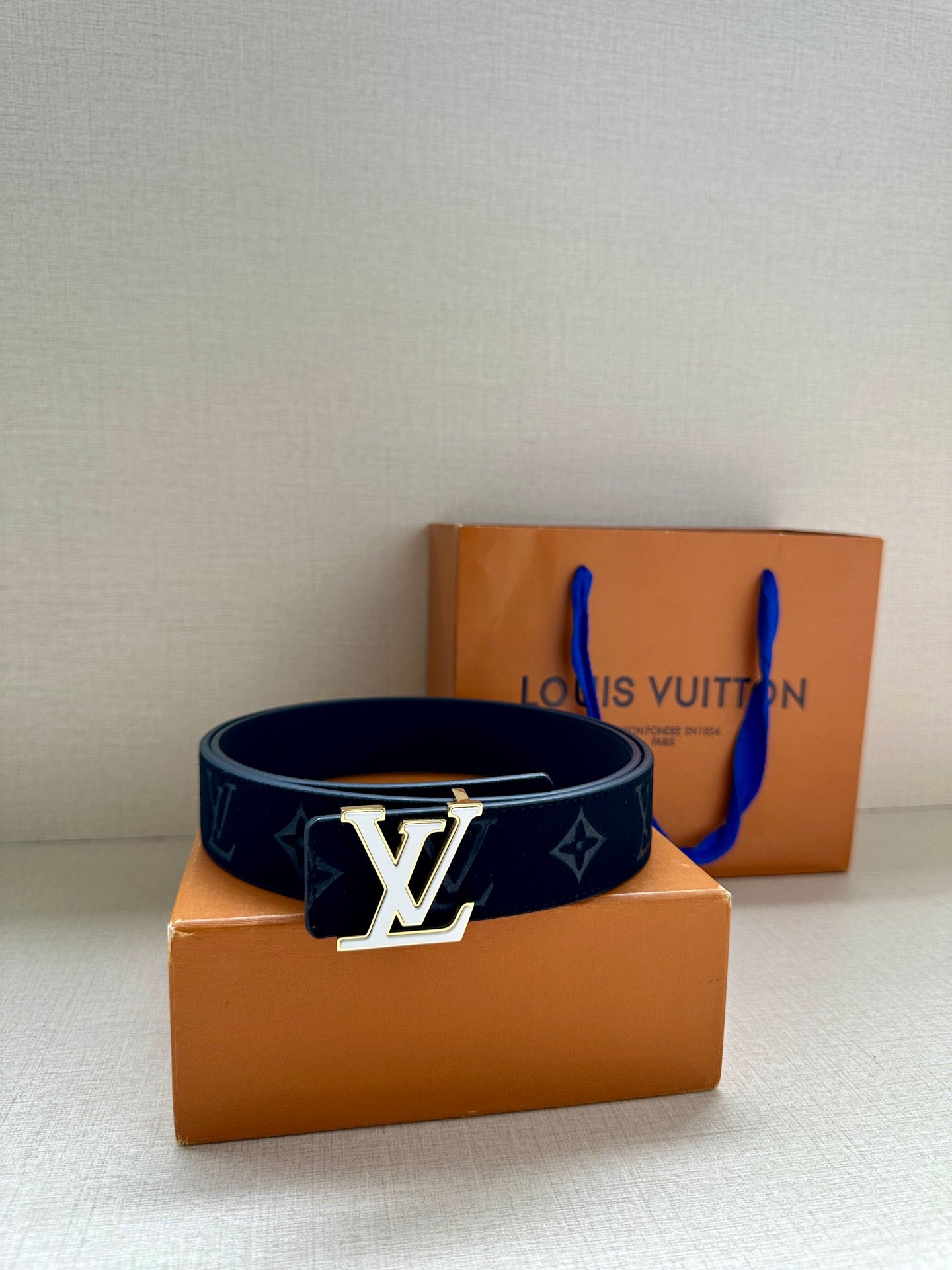Dark navy monogram belt with gold-tone LV buckle resting on boxes