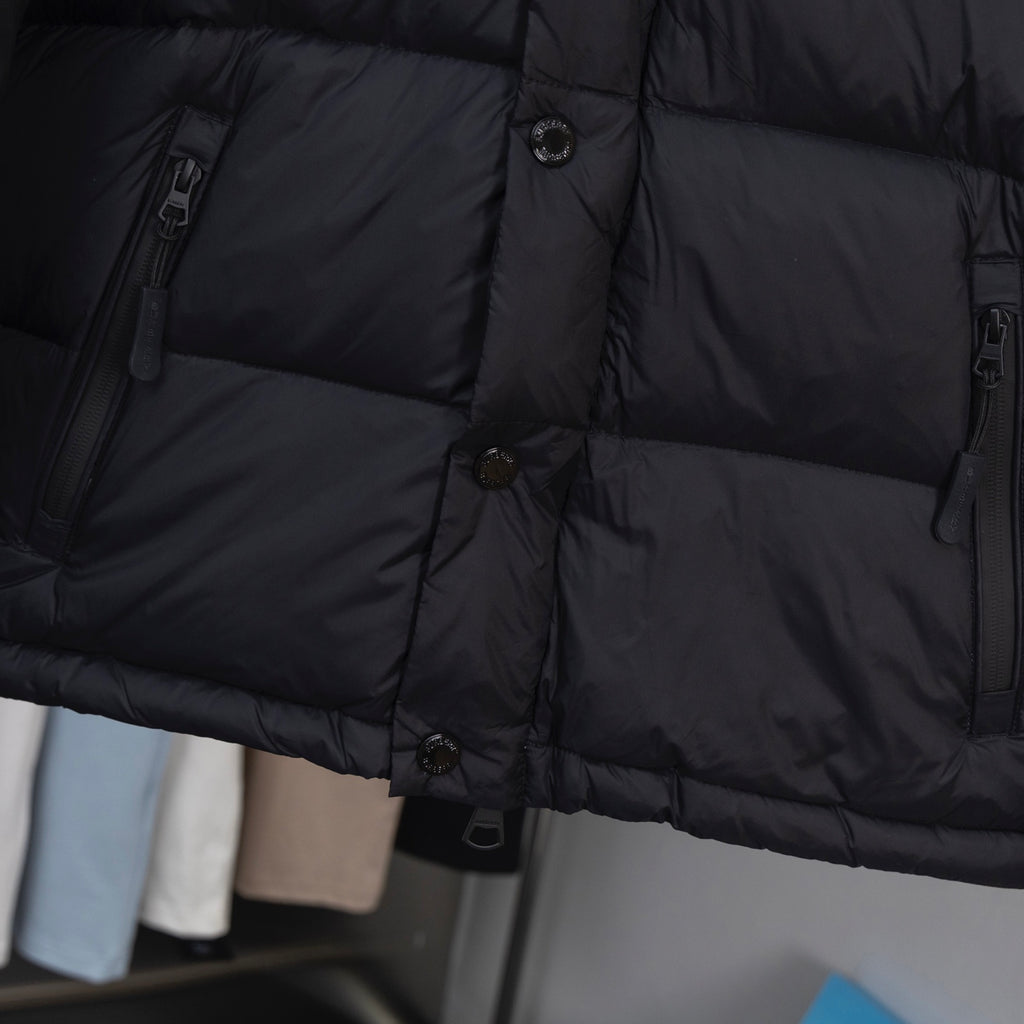 Black puffer jacket fabric close-up with horizontal quilted panels and buttons