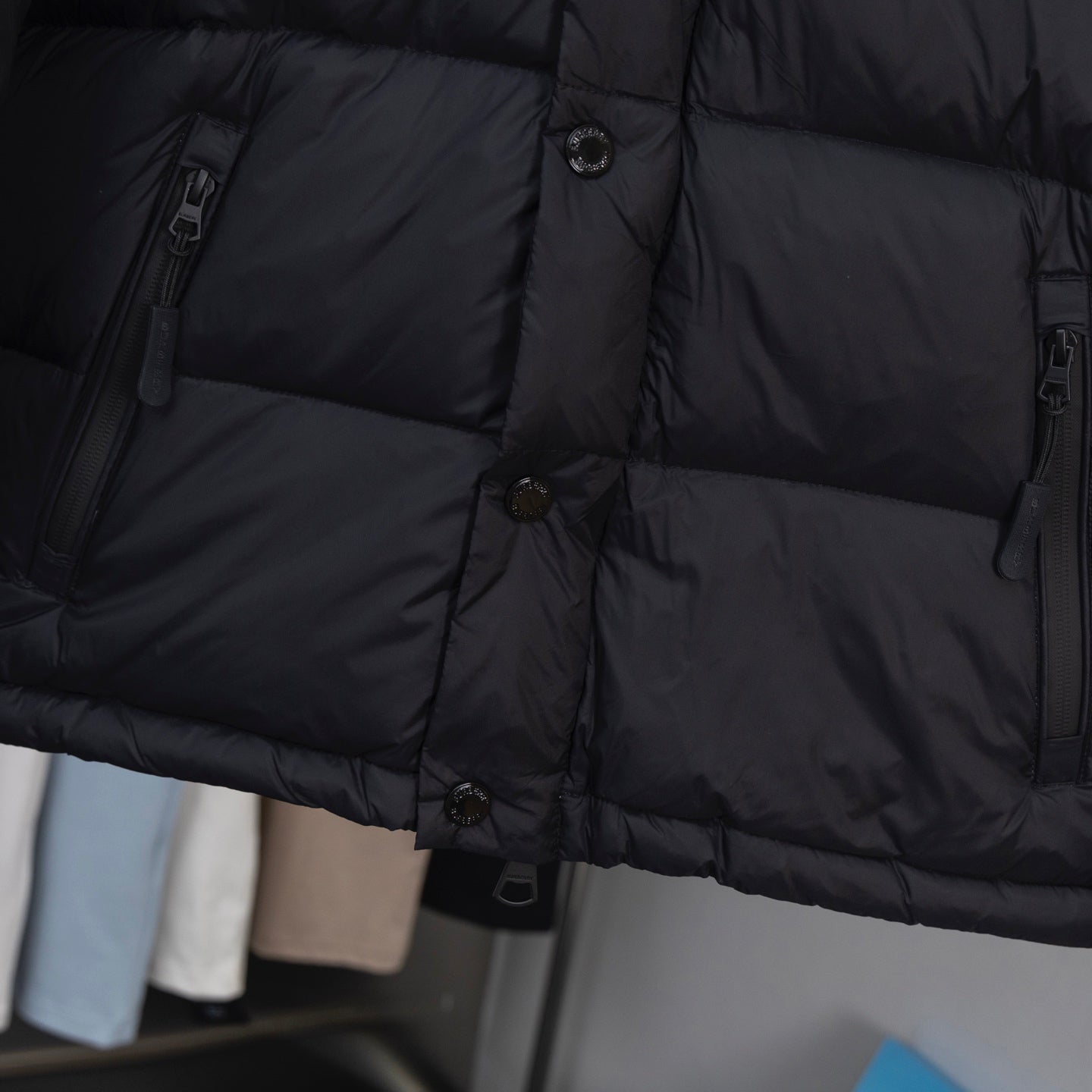 Black puffer jacket fabric close-up with horizontal quilted panels and buttons