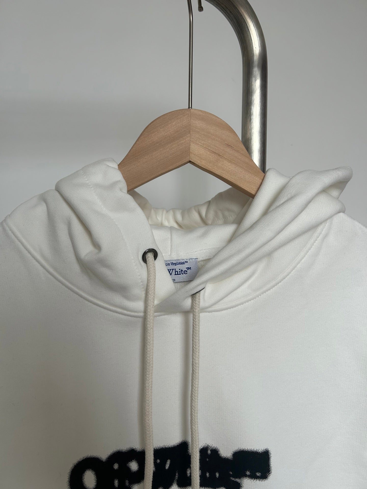 Off-white hoodie close-up at collar with drawstring hood and black logo graphic