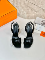 Black heeled sandals with T-strap design and adjustable buckle on box
