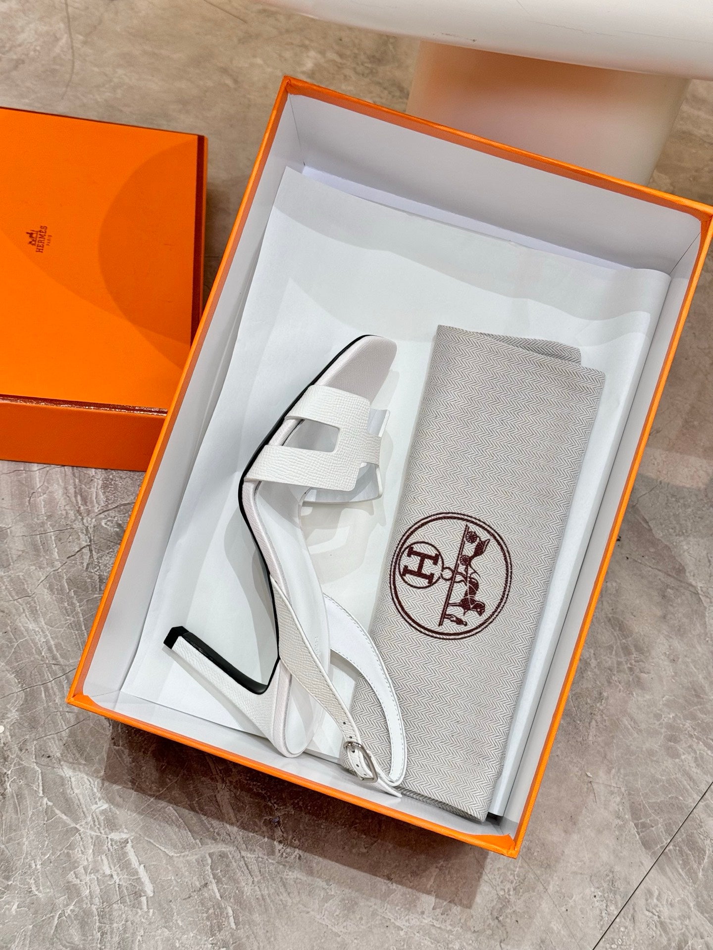 White heeled sandals resting in box, ankle strap and open-toe design