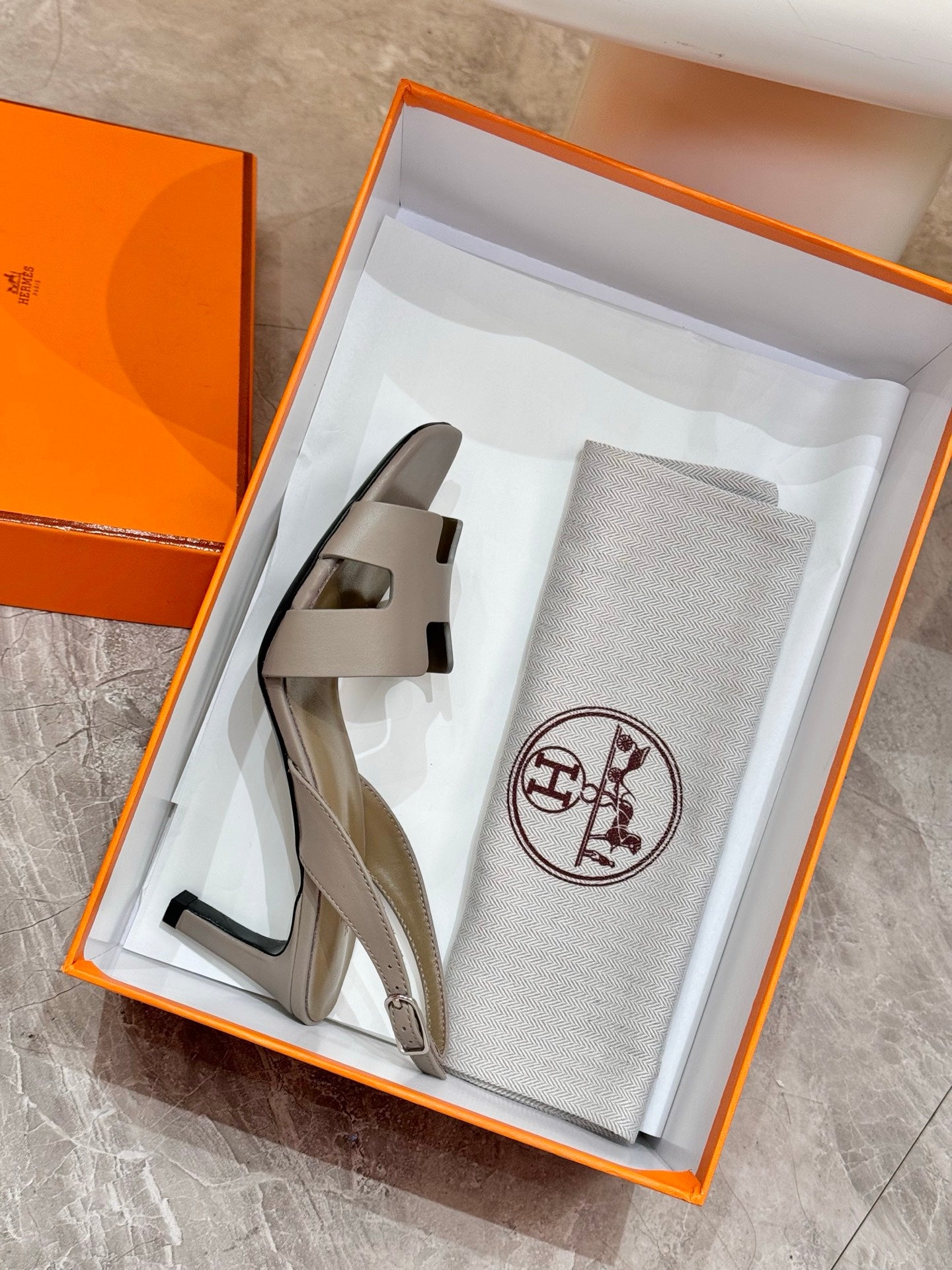 Women’s heeled sandals and Hermes dust bag in an open orange gift box
