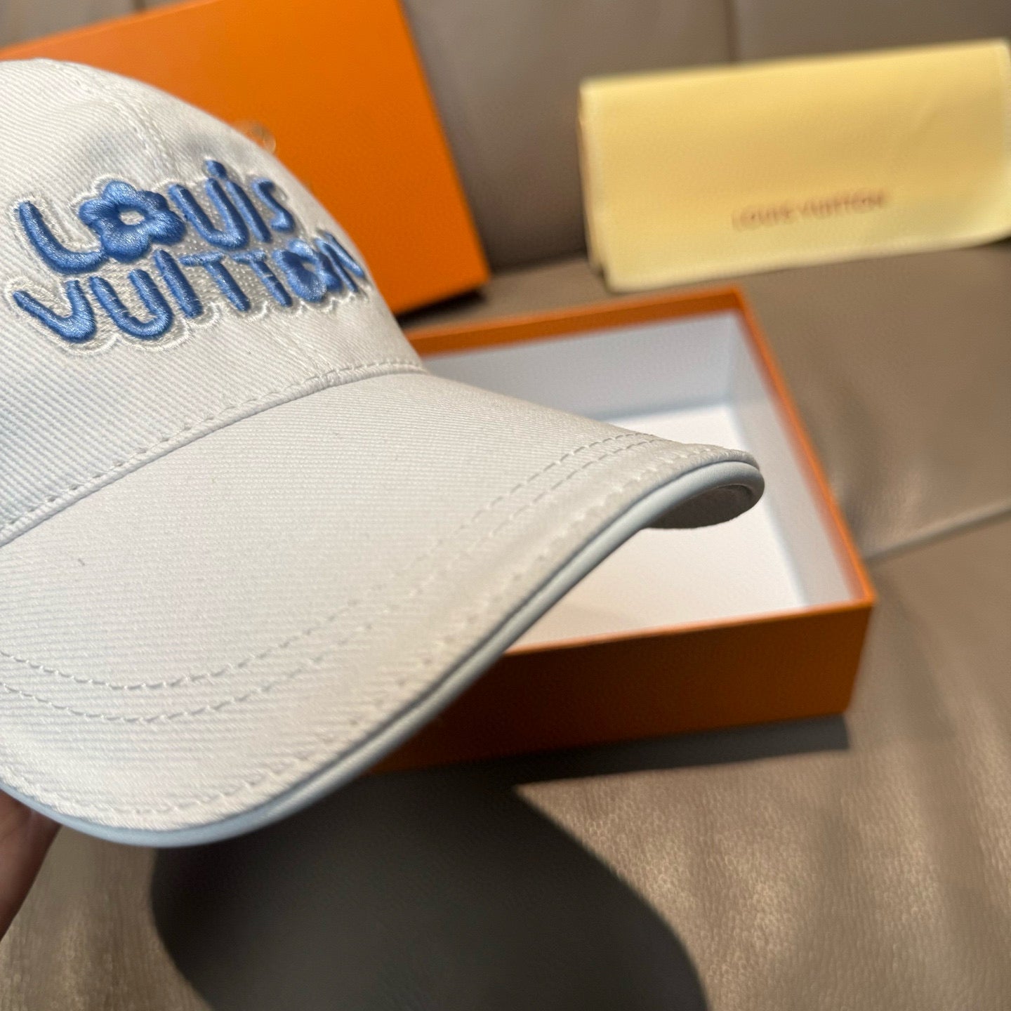 Louis Vuitton white cap close-up showing blue logo and curved brim stitching