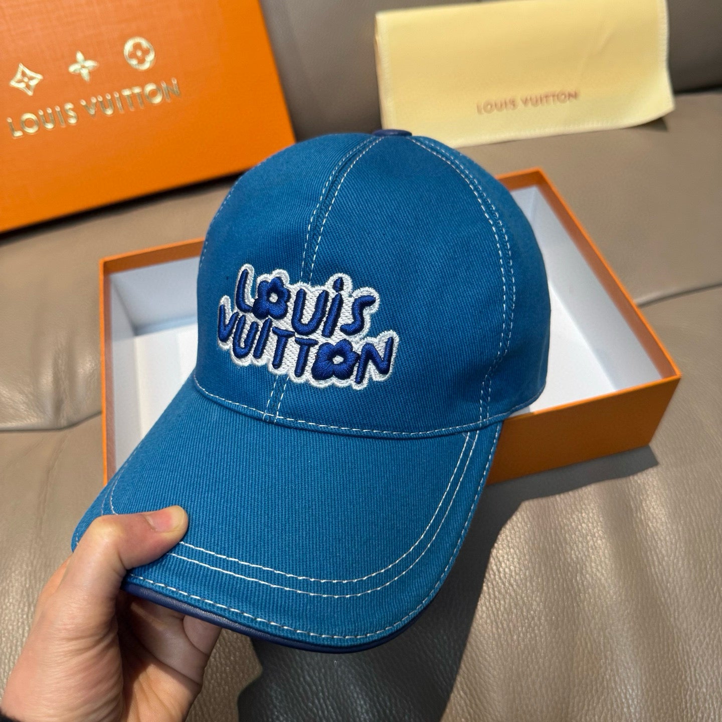 Blue denim cap with curved brim and embroidered Louis Vuitton logo, held in hand
