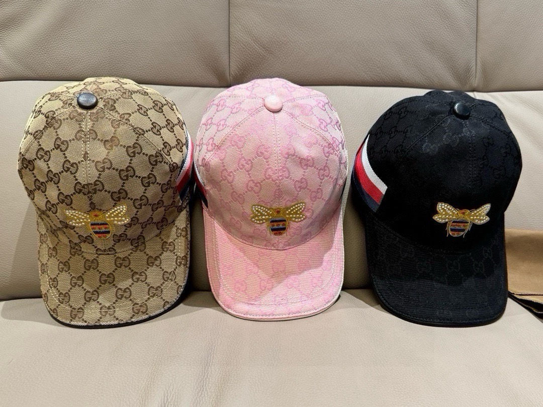 Three baseball caps: tan GG monogram, pink logo, and black with bee patch