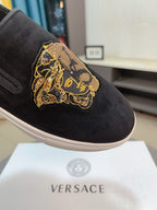 Black suede slip-on sneakers, close-up of gold embroidered crest patch