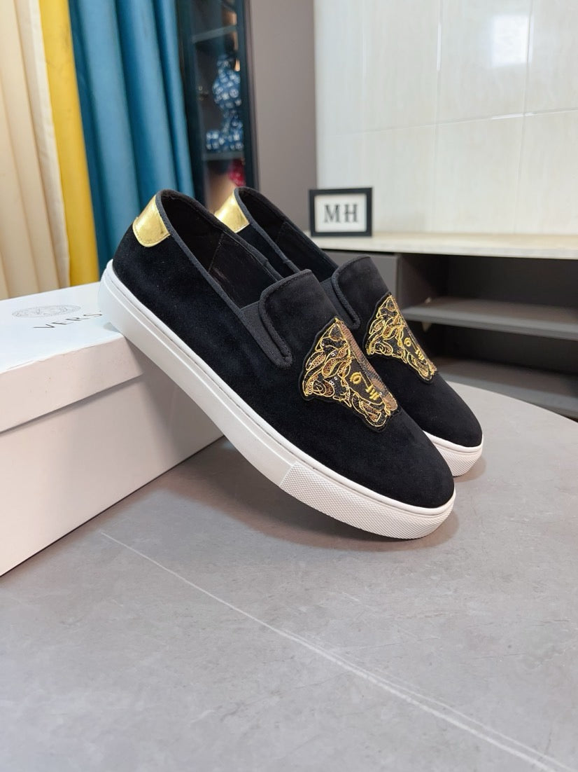 Black suede slip-on sneakers with gold embroidered patch and white rubber sole