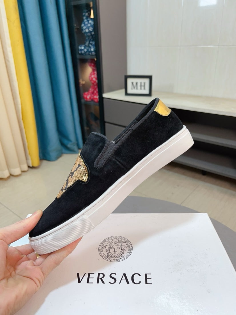 Black suede slip-on sneakers with gold patch and yellow heel tab, angled side view