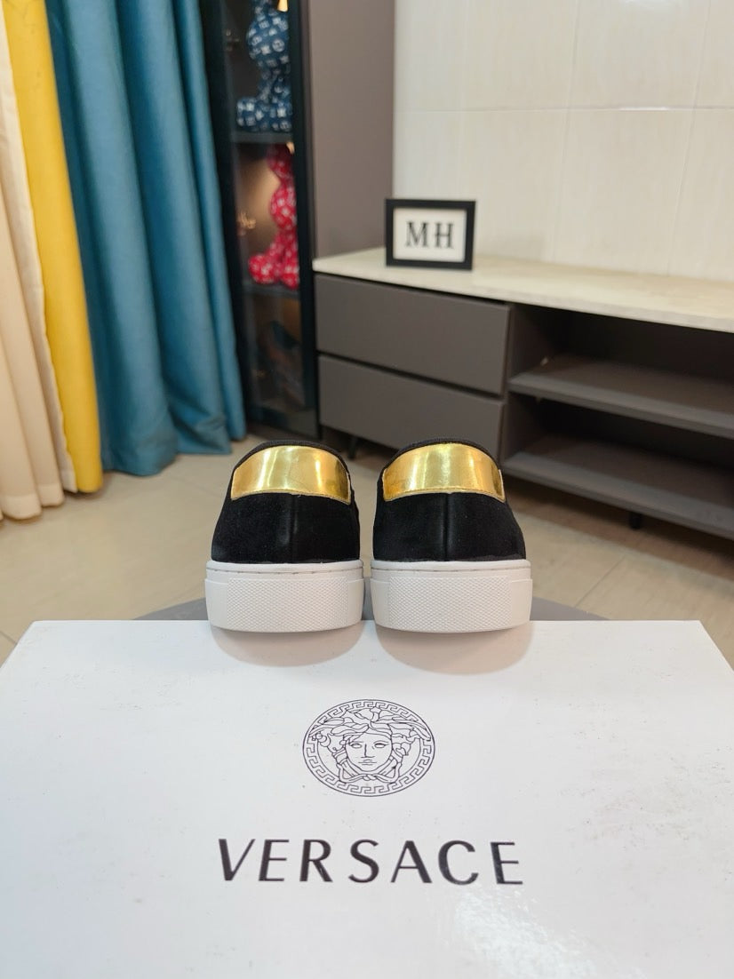 Black suede slip-on sneakers with glossy gold heel caps, rear view