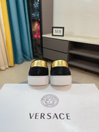 Black suede slip-on sneakers with glossy gold heel caps, rear view