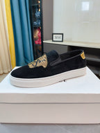 Black suede slip-on sneakers with gold Medusa-style patch, yellow trim, white sole