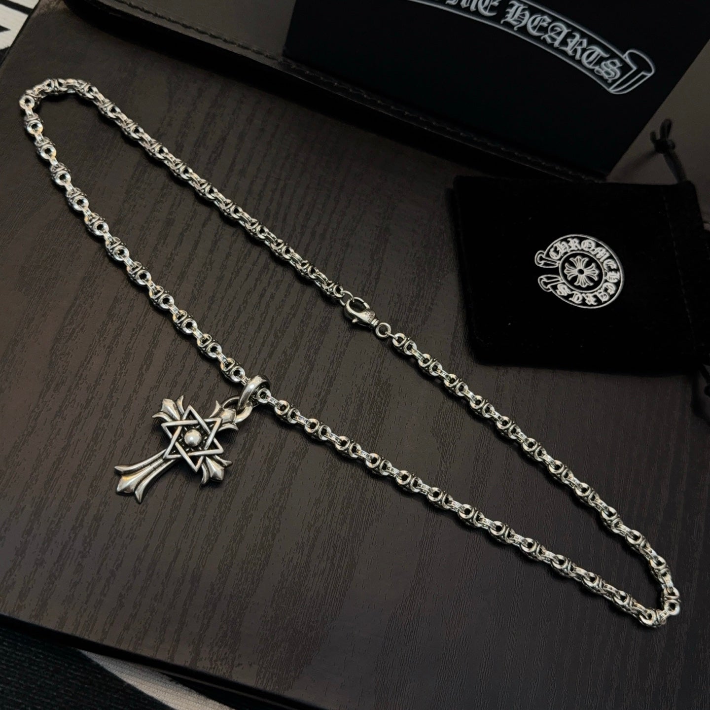 Chrome cross pendant necklaces with long linked chains, laid on a display surface