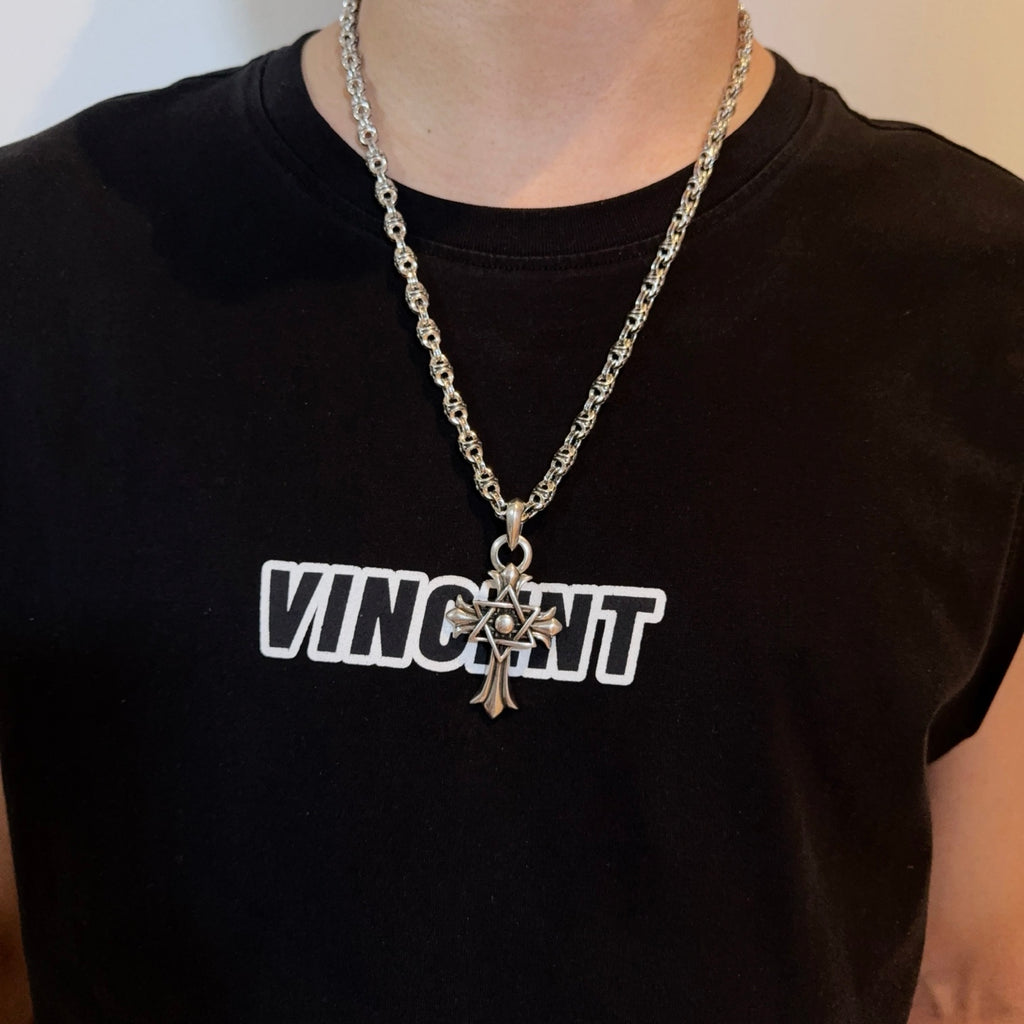 Chrome star-and-cross pendant necklace worn on a dark crewneck shirt