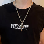 Chrome star-and-cross pendant necklace worn on a dark crewneck shirt