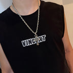 Chrome star-and-cross pendant necklace worn on a sleeveless dark top