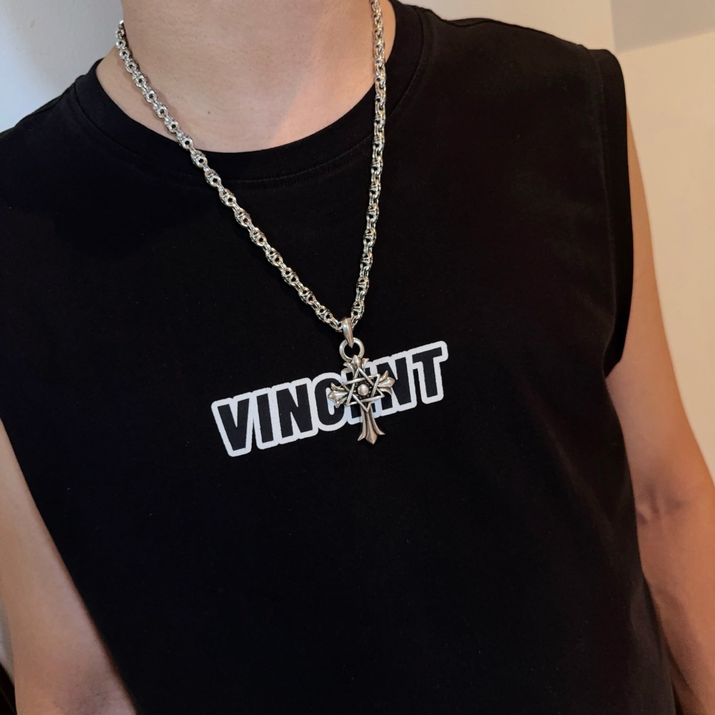 Chrome star-and-cross pendant necklace worn on a sleeveless dark top