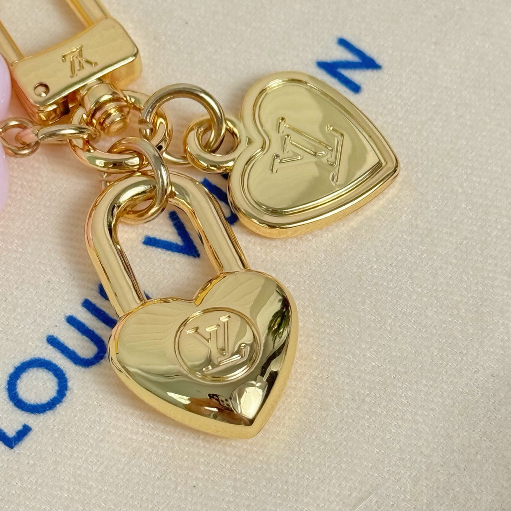 Gold heart and lock charms with blue logo marks on white pouch