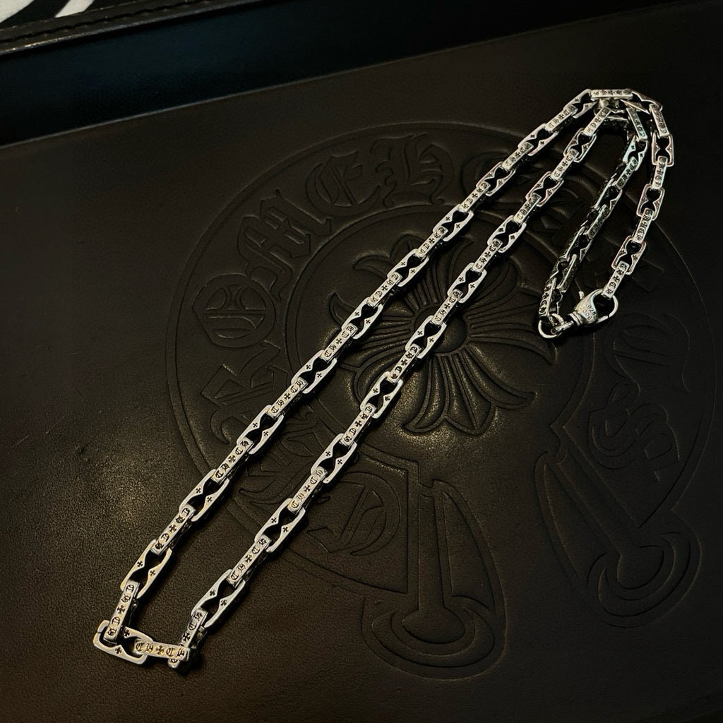 Silver chain necklace laid across dark leather-like surface with embossed pattern