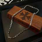 Silver chain necklace draped over wooden display box with butterfly emblem