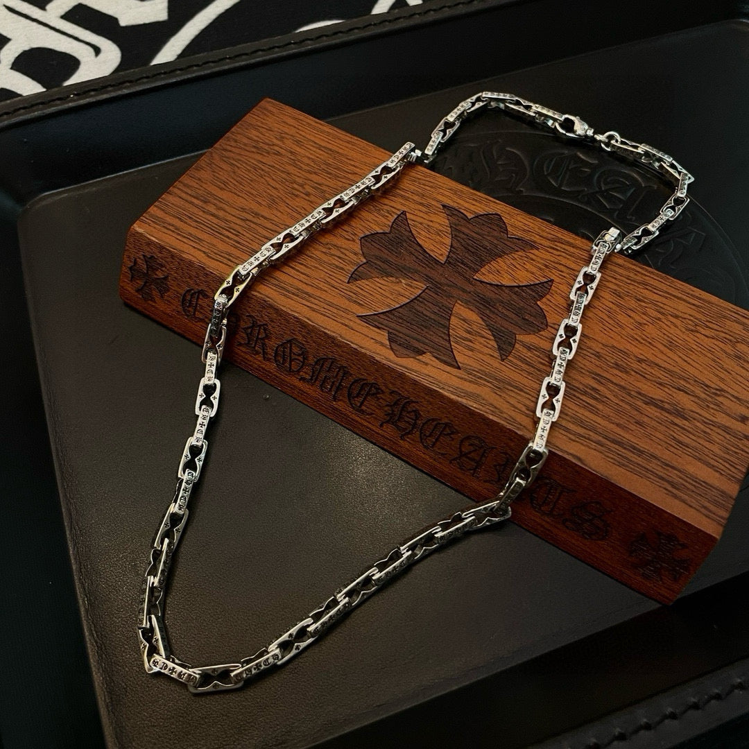 Silver chain necklace draped over wooden display box with butterfly emblem